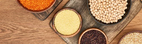 Panoramic shot of bowls with couscous, red lentil, chickpea and black quinoa on wooden cutting boards — Stock Photo