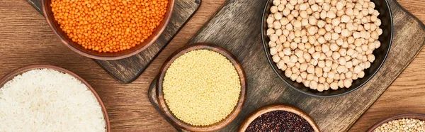 Panoramic shot of bowls with white rice, red lentil, couscous and chickpea on wooden cutting boards — Stock Photo