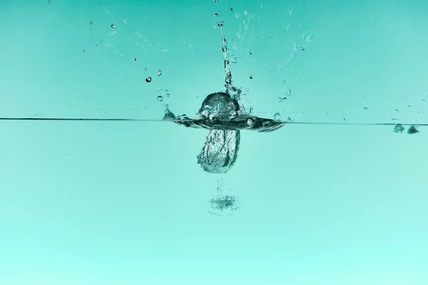 Cubos de gelo transparentes caindo profundamente na água com respingo no fundo turquesa — Fotografia de Stock