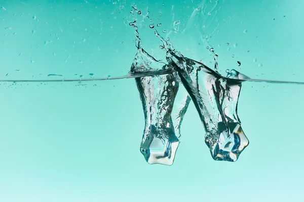 Glaçons tombant dans l'eau avec éclaboussure sur fond turquoise — Photo de stock