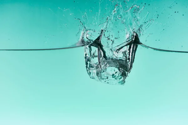 Transparente Eiswürfel, die ins Wasser fallen, mit Spritzer auf türkisfarbenem Hintergrund — Stockfoto