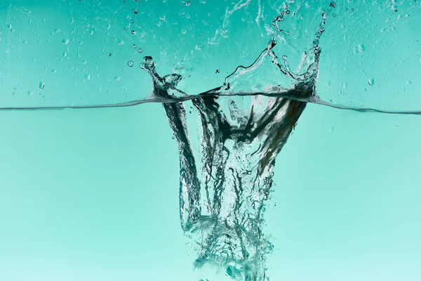 Klare Eiswürfel fallen tief ins Wasser mit Spritzer auf türkisfarbenem Hintergrund — Stockfoto