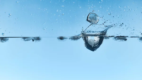 Agua transparente con cubitos de hielo que caen y salpicaduras sobre fondo azul - foto de stock