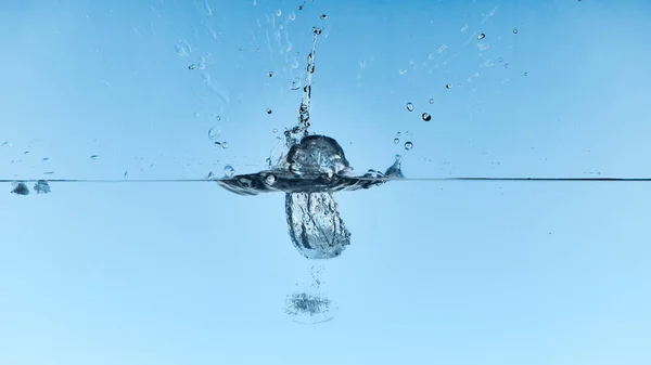 Agua clara con cubitos de hielo cayendo y salpicaduras sobre fondo azul - foto de stock