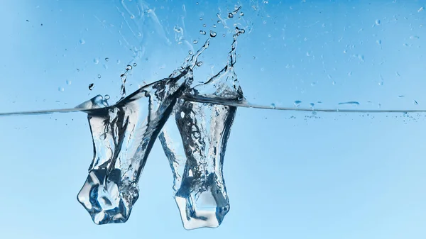 Agua clara con cubitos de hielo cayendo y salpicaduras sobre fondo azul - foto de stock