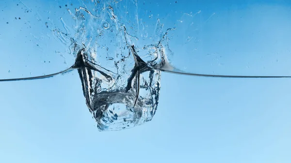 Klares Wasser mit fallenden Eiswürfeln und Spritzwasser auf blauem Hintergrund — Stockfoto
