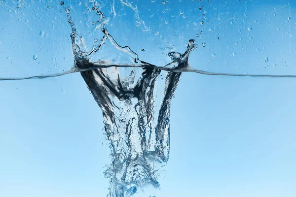 Agua clara con cubitos de hielo cayendo y salpicaduras sobre fondo azul - foto de stock