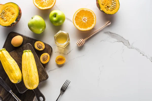 Vista superior de tablas de cortar de madera con calabacín, albaricoques, amarillo, calabaza y miel con cubiertos en la superficie de mármol — Stock Photo