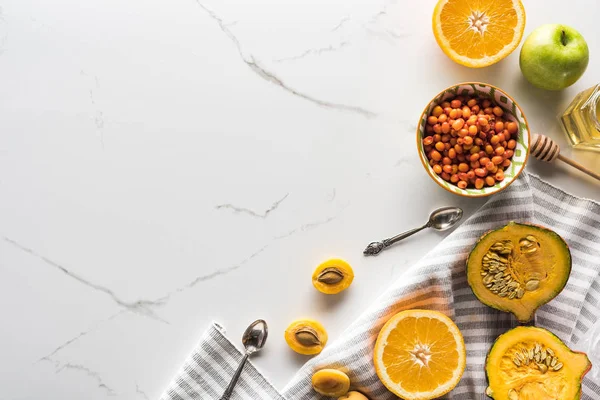 Vista dall'alto di asciugamano a strisce con zucca, albicocche, mela e arancia vicino ciotola con olivello spinoso sulla superficie di marmo — Foto stock