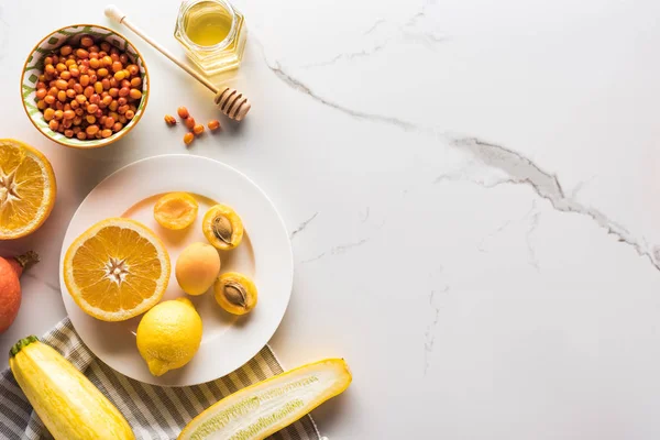 Top view of plate with orange, apricots, lemon, zucchini6 berries and honey on marble surface — Stock Photo