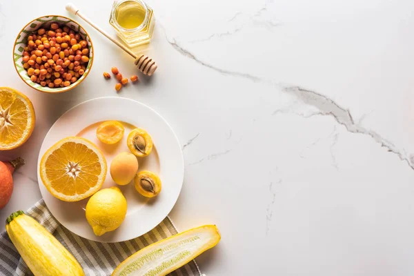 Vista superior del plato con naranja, albaricoques, limón, calabacín 6 bayas y miel en la superficie de mármol - foto de stock