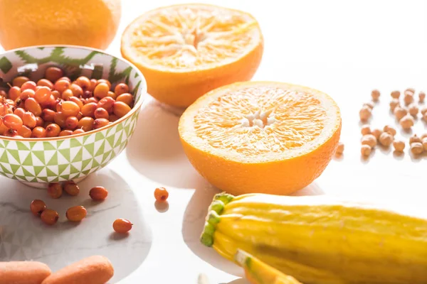 Апельсиновые половинки возле чаши с ягодами и цуккини на мраморной поверхности — стоковое фото