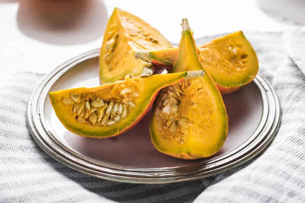 Plate with raw pumpkin quarters on striped towel — Stock Photo