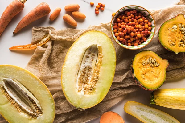 Vista superior de las mitades de melón, bol con bayas, zanahorias y calabacín sobre lienzo - foto de stock