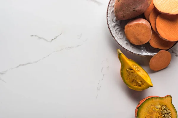 Вид зверху тарілки зі скибочками солодкої картоплі біля шматочків гарбуза на мармуровій поверхні — стокове фото