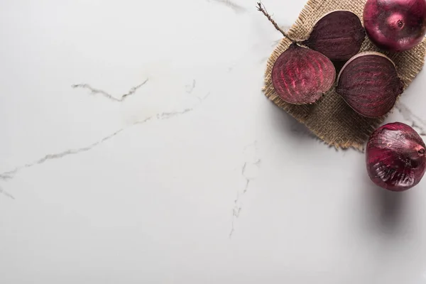 Draufsicht auf rote Zwiebeln und Rote-Beete-Hälften auf Marmoroberfläche mit hessischer — Stockfoto