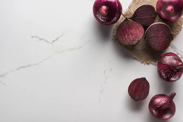 Vista dall'alto di cipolle rosse e barbabietole su superficie di marmo con hessian — Foto stock