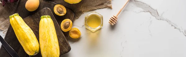 Colpo panoramico di taglieri con zucchine, albicocche e miele sulla superficie di marmo — Foto stock