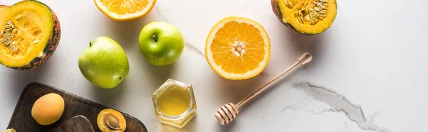 Панорамний знімок обробних дощок з гарбузом, апельсином, абрикосами та медом на мармуровій поверхні — стокове фото