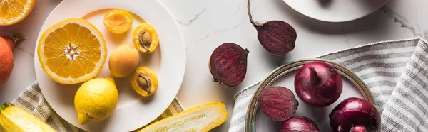 Plano panorámico de platos con frutas y verduras sobre superficie de mármol con textil a rayas - foto de stock