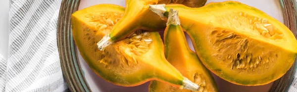 Panoramic shot of pumpkin quarters on plate near striped textile — Stock Photo