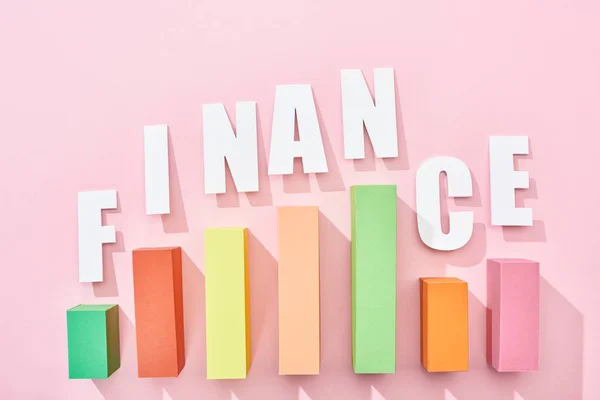 Top view of white finance inscription with color block graph on pink background — Stock Photo