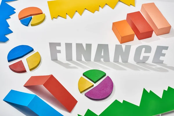 Финансовая надпись возле многоцветных блоков и круговых диаграмм с тенью на белом фоне — стоковое фото