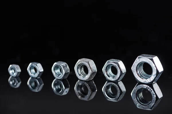 Row of brand new shiny metallic nuts isolated on black — Stock Photo