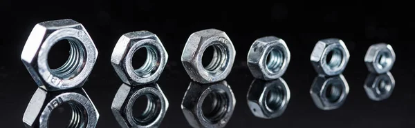 Panoramic shot of shiny metallic nuts row isolated on black — Stock Photo