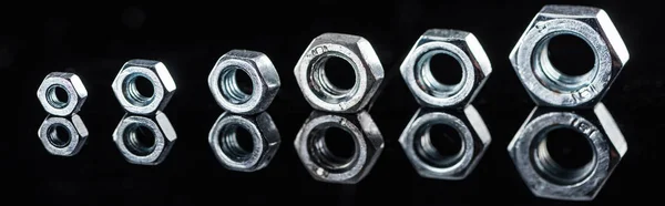Panoramic shot of shiny new metallic nuts isolated on black — Stock Photo