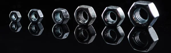 Panoramic shot of shiny steel nuts row isolated on black — Stock Photo