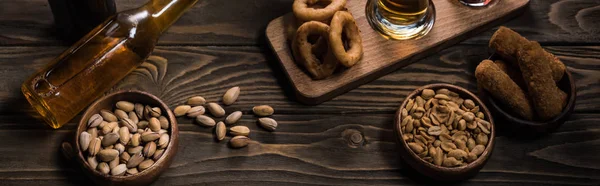 Plano panorámico de botella de cerveza ligera cerca de cuencos con aperitivos en mesa de madera - foto de stock