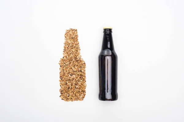 Vue du dessus de la bouteille de bière noire près de grains de blé entier isolés sur blanc — Photo de stock
