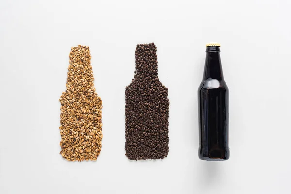 Вид зверху пляшки темного пива біля пшениці та зерна кави ізольовані на білому — стокове фото
