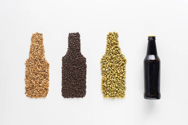 Верхний вид бутылки темного пива возле пшеницы, зерна кофе и прессованный хмель изолированы на белом — стоковое фото