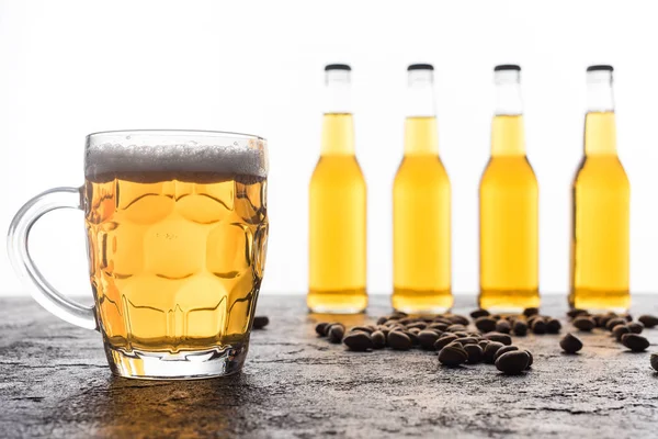 Mug with light beer near bottles and coffee grains on brown textured surface — Stock Photo