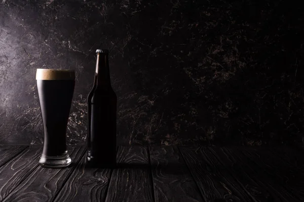 Vidro e garrafa de cerveja escura na mesa de madeira com sombra — Fotografia de Stock