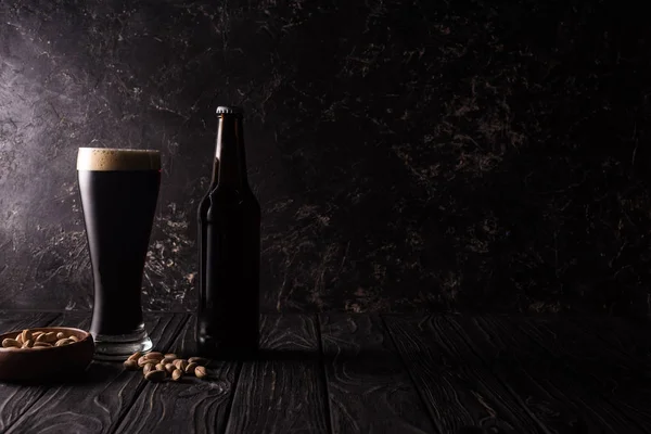 Vidro e garrafa de cerveja perto da tigela com pistache na mesa de madeira — Fotografia de Stock