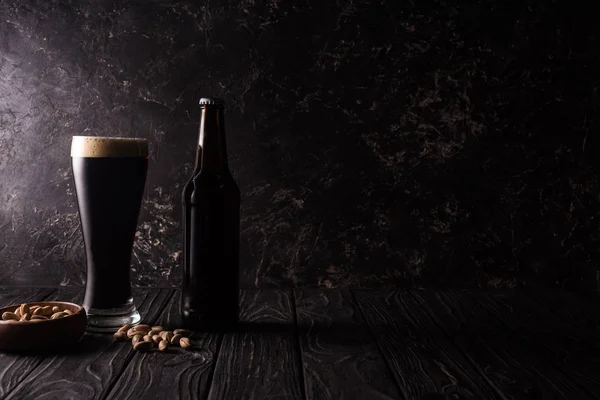 Vaso y botella de cerveza cerca del tazón con pistachos en la mesa de madera - foto de stock