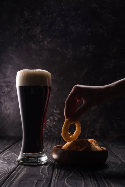 Cropped view of man taking fried onion ring near glass of beer on wooden table — Stock Photo