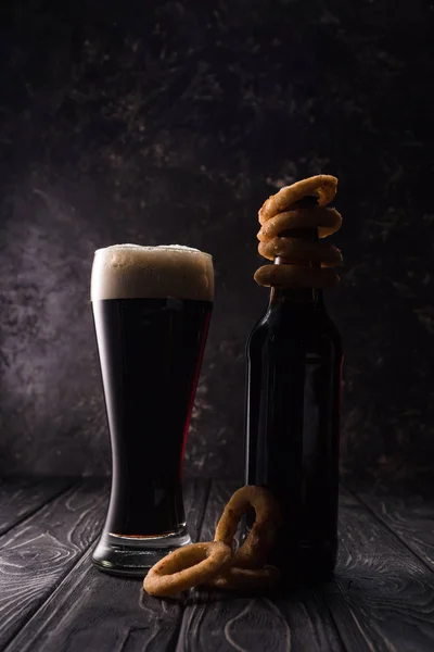 Bicchiere e bottiglia di birra con anelli di cipolla fritta sul tavolo di legno — Foto stock