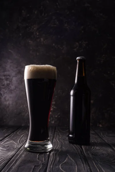 Bottle near glass of beer on wooden table — Stock Photo