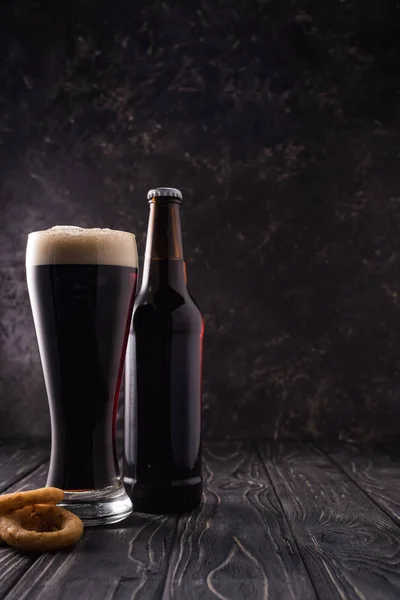 Бутылка и стакан пива возле жареных луковых колец на деревянном столе — стоковое фото