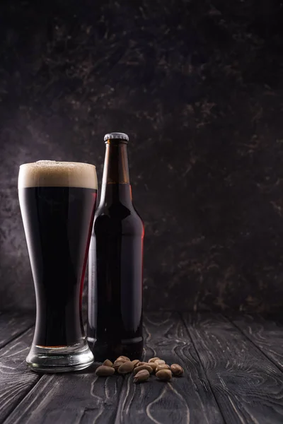 Flasche und Glas Bier neben Pistazien auf Holztisch — Stockfoto