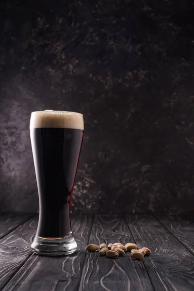 Verre de bière avec mousse près des pistaches sur table en bois — Photo de stock