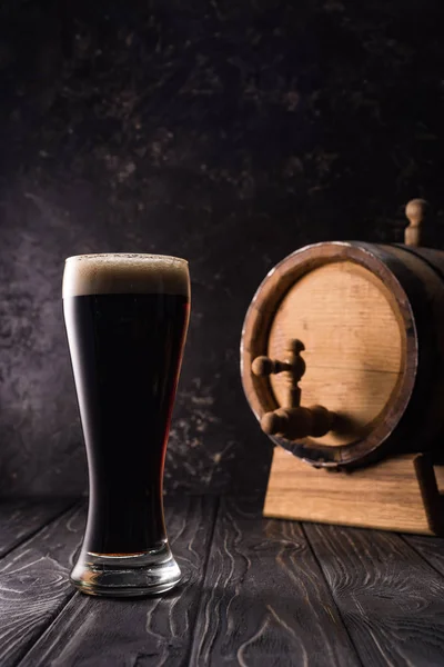 Vaso de cerveza cerca de barril marrón pequeño con grifo en la mesa de madera - foto de stock