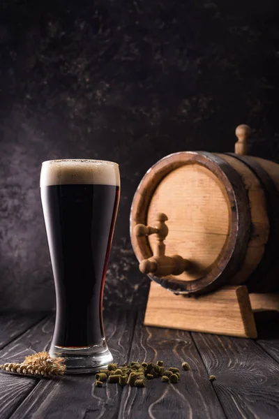 Стакан пива возле колосьев пшеницы и небольшой бочонок с краном на деревянном столе — стоковое фото