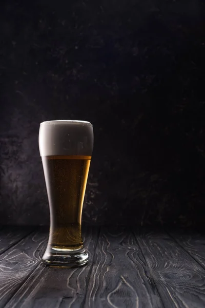 Verre de bière légère fraîche avec mousse sur table en bois — Photo de stock