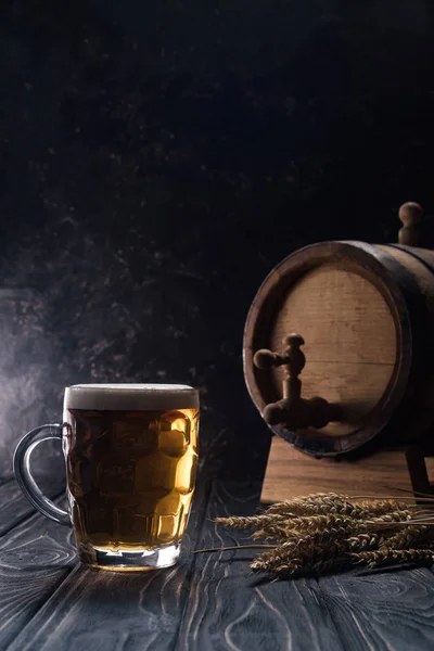 Mug of light beer near small keg and wheat spikes on wooden table — Stock Photo