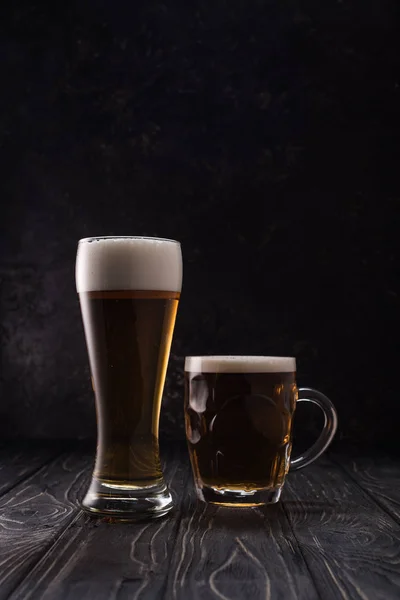 Glass and mug of fresh light beer with foam on wooden table — Stock Photo